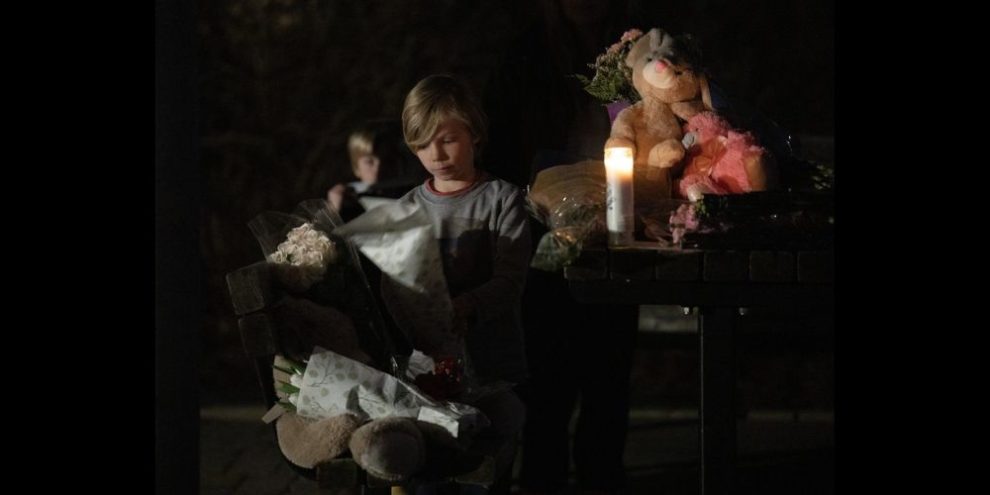 A child places flowers on a park table where flowers and teddy bears had been placed during a vigil for the six people killed on March 7 in Ottawa. THE CANADIAN PRESS/Adrian Wyld