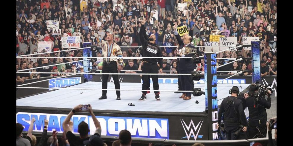 This undated photo provided by the WWE shows from left, Dwayne "The Rock" Johnson, Roman Reigns and Paul Heyman in the ring during WWE Smackdown. As WWE gears up for its biggest annual premium live event in April 2024, the company continues to harness the power of its social media presence to reach its fans. A key component of that strategy is YouTube, where WWE has hit an important milestone: reaching 100 million subscribers. (Scott Brinegar/WWE via AP)