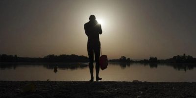 A man prepares to enter the water as the sun rises above the Miribel lake, outside Lyon, France, June 18, 2022 - AP