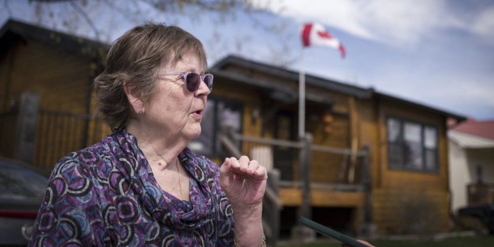 A woman in front of a house waving the Canadian flag.