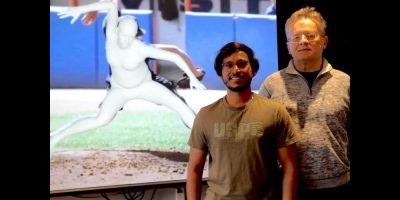 Two men stand in front of an animation of a pitching motion.