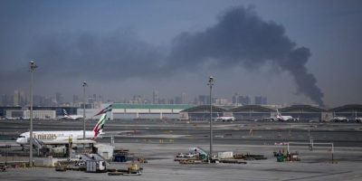 Smoke rises in the distance as Emirates planes sit on the tarmac at Dubai International Airport after Iranian strikes led to airspace closures.