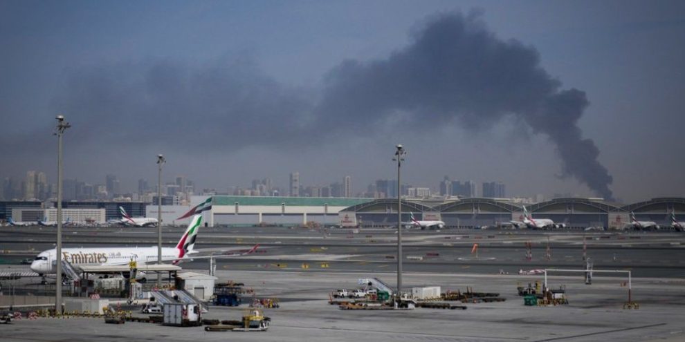 Smoke rises in the distance as Emirates planes sit on the tarmac at Dubai International Airport after Iranian strikes led to airspace closures.