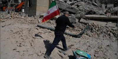 A man carries an Iranian flag to place on rubble at a damaged police facility in Tehran following U.S.-Israeli airstrikes on March 4, 2026.