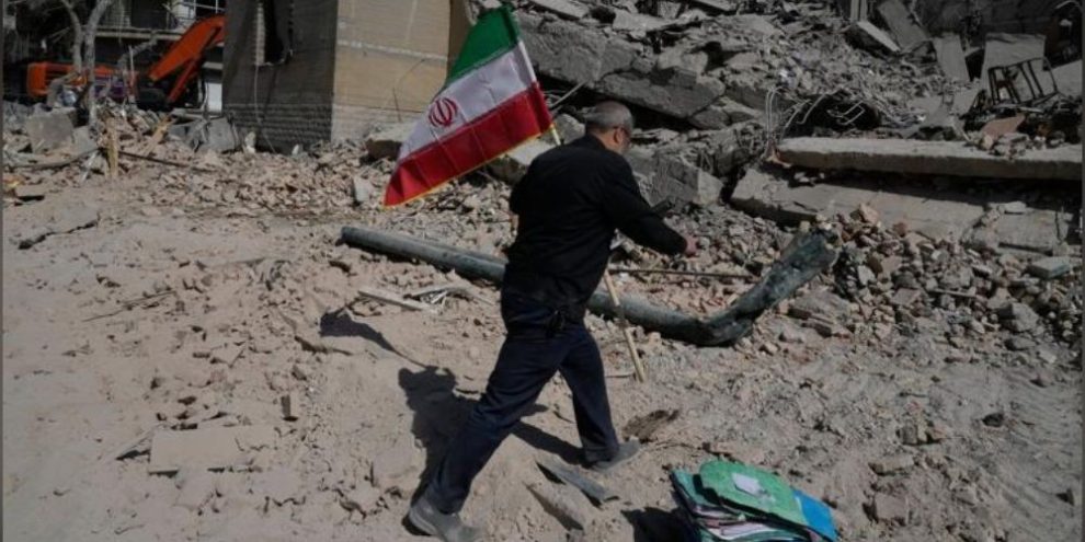 A man carries an Iranian flag to place on rubble at a damaged police facility in Tehran following U.S.-Israeli airstrikes on March 4, 2026.