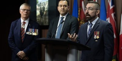 Former Chief of the Defence Staff Rick Hillier and Conservative MP Blake Richards stand beside Valour in the Presence of the Enemy founder Bruce Moncur during a press conference on Parliament Hill in Ottawa on Wednesday, April 15, 2026.