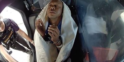 Tiger Woods handcuffed and seated in a police vehicle after a DUI arrest following a car crash in Florida, as seen in body camera footage.
