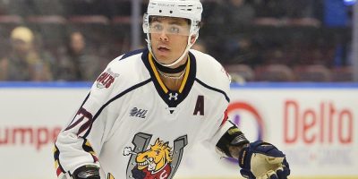 Barrie Colts defenceman Kashawn Aitcheson skating with the puck during an OHL game, wearing his team uniform and helmet, focused on play.