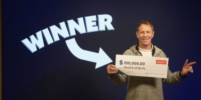 David B. of Barrie holds oversized $100,000 cheque after claiming Instant Crossword Tripler lottery prize at OLG Prize Centre in Toronto.