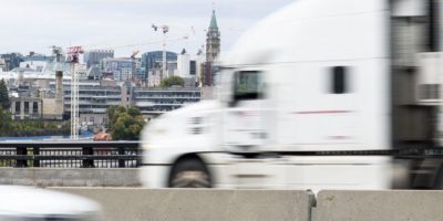 Long-haul transport truck travelling on the Ontario-bound side of the Macdonald-Cartier Bridge in Ottawa, with roadway and river visible in the background.