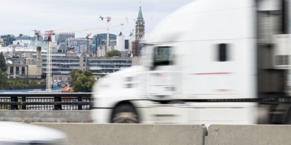 Long-haul transport truck travelling on the Ontario-bound side of the Macdonald-Cartier Bridge in Ottawa, with roadway and river visible in the background.