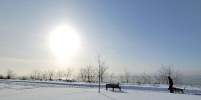 A person walking a dog on a trail overlooking Lake Ontario in Newcastle, Ontario