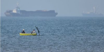 Two men in a small boat with cargo ships anchored in the Strait of Hormuz near Bandar Abbas, Iran
