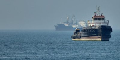 Cargo ships anchored in the Strait of Hormuz near Bandar Abbas, Iran, with an Iranian tugboat in the foreground