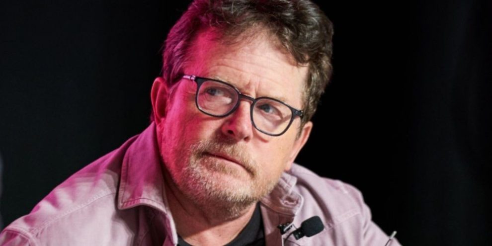 Michael J. Fox speaking at an event marking the 40th anniversary of the film Back to the Future in Toronto, standing at a podium with a microphone during a public appearance.
