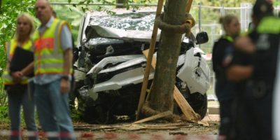 Police officers stand near a vehicle that crashed into a tree after a suspected attack near Berlin’s Pride event.