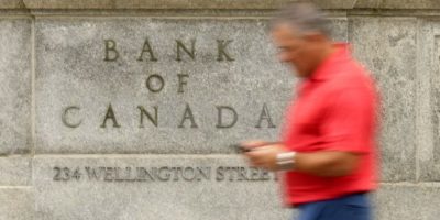 Man checks his phone while walking past the Bank of Canada building in Ottawa