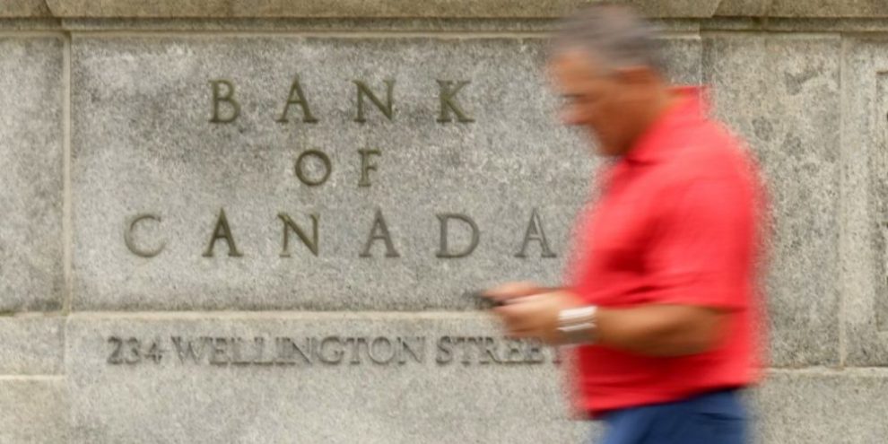Man checks his phone while walking past the Bank of Canada building in Ottawa