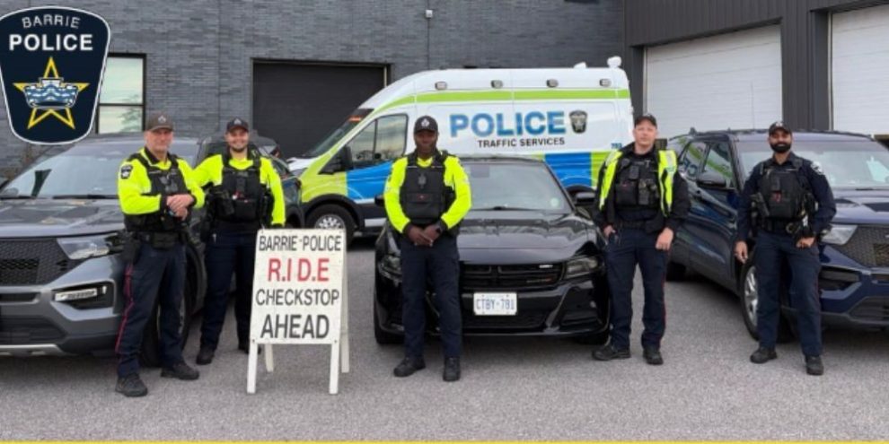 Barrie Police officers stand in front of police vehicles and a RIDE sign at Barrie Police headquarters.