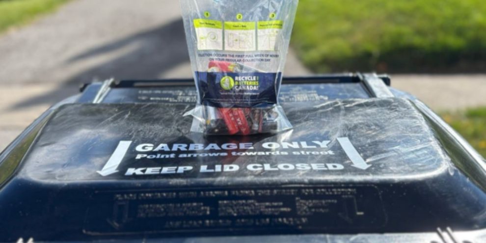 Bag of used household batteries placed on top of a curbside waste bin for collection.